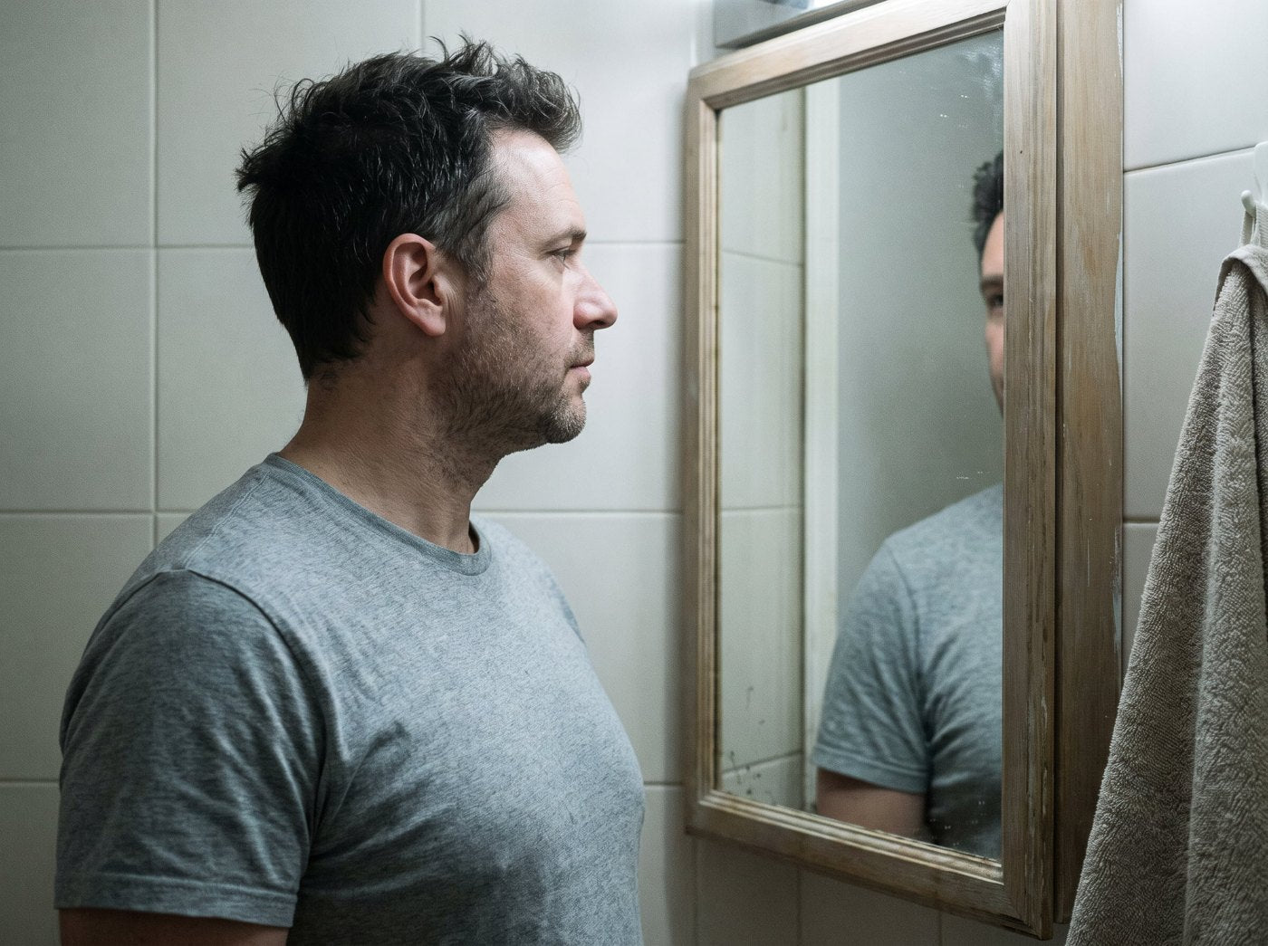 A man standing at a bathroom mirror in the morning